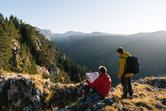 Two men reading a map sat on top of a mountain