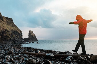 Person in red coat walking along rocky beach
