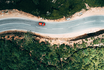 aerial shot of red car driving down windy road