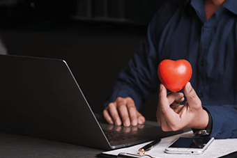 man on laptop holding heart-shaped balloon in hand