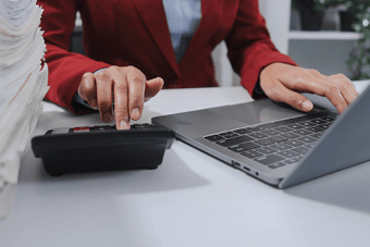 woman typing on calculator next to stack of papers