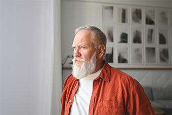 Older man in red jacket looking out of a window