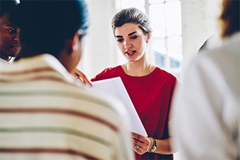 woman with a red jumper on reading in a meeting with two other people