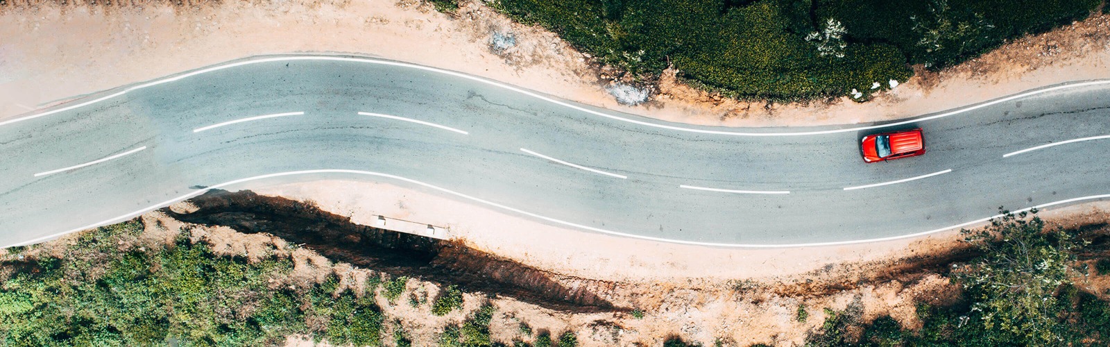 aerial shot of red car driving down windy road